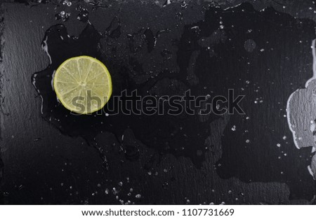 Lemon slice on black stone plate with water splash, top view