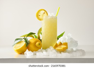 Lemon slush in tall glass with fruit and crushed ice around it on white table with isolated background. Front view. Horizontal composition.