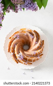 Lemon, Vanilla Bundt Cake With Sugar Glaze And Lilac Flowers On A White Background. Spring Composition. Deliciuos Homemade Easter Sponge Cake. Confectionery, Bakery Menu. Top View, Flat Lay