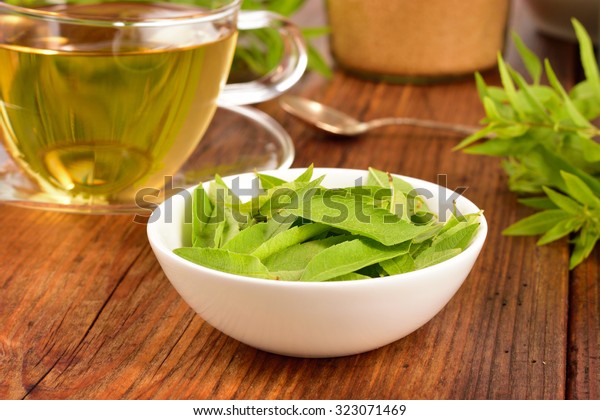 Lemon verbena leaves on white bowl and\
verbena tea on wooden table. Aloysia\
citrodora.