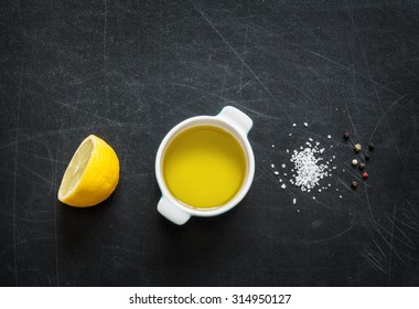 Lemon Vinaigrette Dressing Ingredients On Black Chalkboard Background From Above. Lemon, Olive Oil, Salt And Pepper. Layout With Free Text Space.