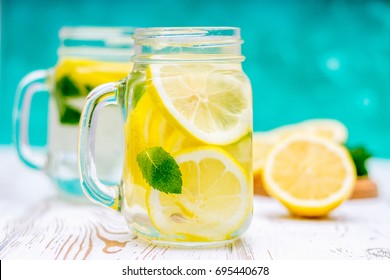 Lemon water, lemonade in mugs with handles, mason jar on a white wooden table. Cut Lemons in the background. Natural lemonade. - Powered by Shutterstock