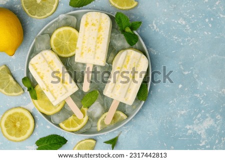 Lemon yogurt ice cream on a stick on a plate with ice, mint and lemon slices on a blue background. Copy space. Top view