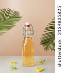 Lemonade in a clear bottle on a light mirror table. Lemon wedges and mint leaves on the table. Malm leaves in the background