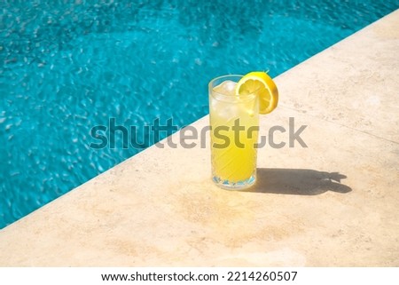Lemonade in glass with fresh lemon slice on the poolside. Summer drink refreshing lemonade, minimal concept.