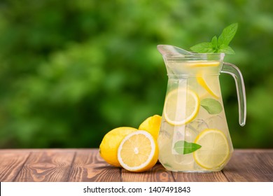 lemonade in glass jug on wooden table outdoors. Summer refreshing drink. Cold detox water with lemon