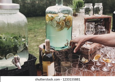 Lemonade jar and glasses for wine,martini, alcohol drinks on wooden table outdoors. Rustic catering at wedding reception. Barn wedding concept. Christmas holiday feast. Cocktail bar