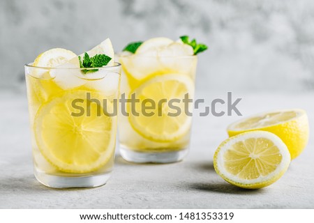 Lemonade with lemon, mint and ice cubes in glass on gray stone background. Cold summer refreshing drink or beverage