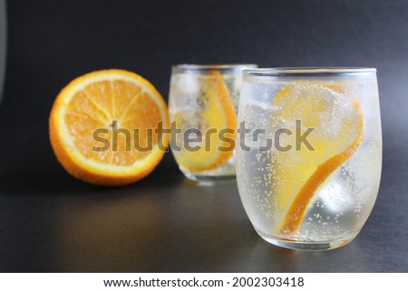 lemonade with orange and ice in a glass on a black background next to lies ice and orange. Summer drink on a black background.