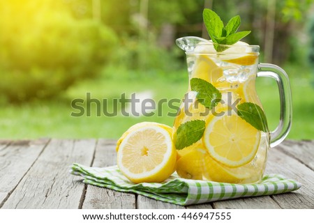 Lemonade pitcher with lemon, mint and ice on garden table. View with copy space