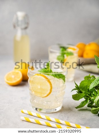 Lemonade soda drink with fresh lemons. Refreshing cocktail with lemon, mint and ice on textured light background. Summer cold drinks concept.