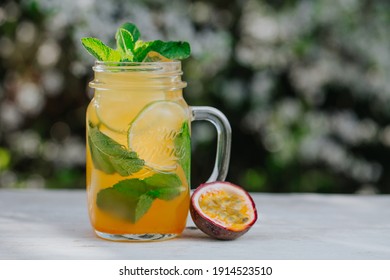 Lemonade or tropical cocktail with lemon, passion fruit, orange and mint, cold refreshing drink or beverage with ice on white table.