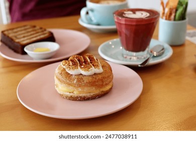 Lemon-filled merengue donut and beetroot velvet latte on a pink plate with background table setting elements - Powered by Shutterstock