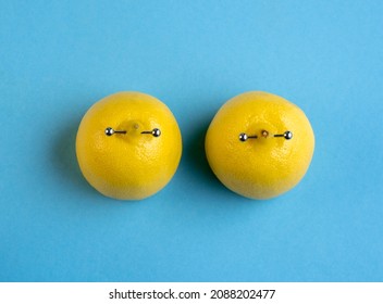 Lemons in shape of woman breast with nipple piercing on blue background. 