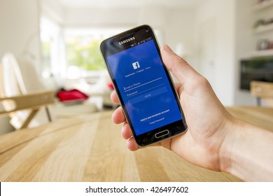 LENDELEDE, BELGIUM - MAY 24TH 2016: a hand holding a Samsung Galaxy S5 mini mobile phone which displays the Facebook app on the touch screen. An illustrative editorial image on an interior background.