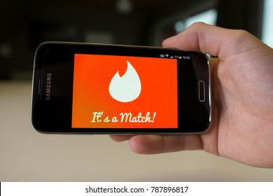 LENDELEDE, BELGIUM - NOVEMBER 28TH 2017: a male hand holding a Samsung Galaxy S5 mini mobile phone which displays a red Tinder match screen. An illustrative editorial image on an interior background.