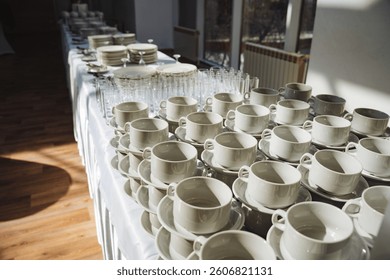 A lengthy table adorned with pristine white cups, delicate saucers, and various exquisite serveware, creating a charming display of elegant dishware and beautifully crafted pottery