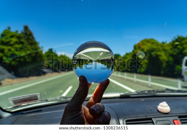 lens ball inside a\
car with a street in the background, crystal glas ball image with\
blue sky and a street