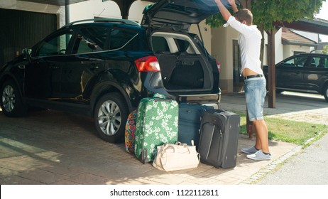 LENS FLARE: Caucasian Man In White Shirt Closes The Trunk Of His Car After Unloading Heavy Travel Bags. Young Male Is Happy After Unpacking All Of His Luggage After Coming Back From Summer Vacation