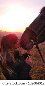 LENS FLARE, CLOSE UP: Caring Young Woman Kisses Her Beautiful Brown Horse On The Muzzle. Cheerful Caucasian Girl Enjoying A Calm Spring Morning In The Countryside With Her Muscular Female Horse.