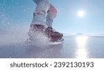 LENS FLARE, CLOSE UP: Flying pieces of crushed ice when guy brakes on skates. Active man is ice skating on a big frozen lake and practicing hockey stop. Beautiful sunny day for winter activities.