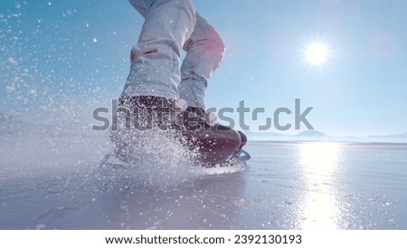 LENS FLARE, CLOSE UP: Flying pieces of crushed ice when guy brakes on skates. Active man is ice skating on a big frozen lake and practicing hockey stop. Beautiful sunny day for winter activities.