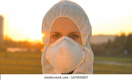 LENS FLARE, CLOSE UP, PORTRAIT, DOF: Young Female Nurse Wears A Protective Suit And Mask During The COVID19 Outbreak In Northern Italy. Female Doctor In Protective Clothing Stands Outside At Sunrise.