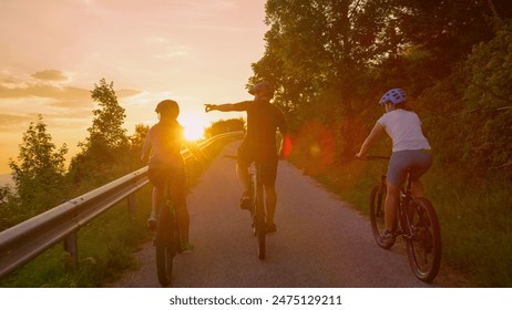 LENS FLARE: Group of cyclists rides their ebikes along the empty country road at sunset. Young tourists enjoy a relaxing bicycle trip across Slovenia on a sunny summer evening. Fun outdoor activity - Powered by Shutterstock