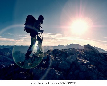 Lens flare light, strong defect. Tourist guide on trekking path  with poles and backpack.  Experienced hiker in windcheater and hood stand on rocky view point above misty valley. Sunny fall day