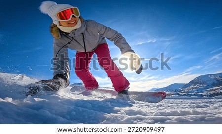 LENS FLARE, LOW ANGLE VIEW, CLOSE UP: Cheerful female snowboarder drags her hand and sprays snow while she carves across a sunlit slope. Winter fun and authentic snowboard action in Austrian Alps.