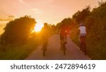 LENS FLARE: Three fit friends enjoy a scenic bicycle journey around the picturesque countryside on an idyllic summer evening. Young travelers explore the rural landscape on electric bikes at sunset.