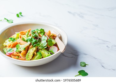 Lentil pasta with broccoli, avocado, radish and sprouts in a white bowl. Healthy vegan recipe concept.