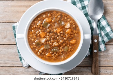 Lentil soup with vegetables in bowl on wooden table. Top view