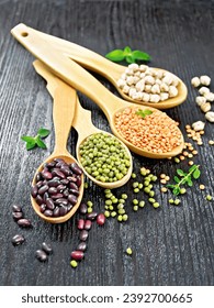 Lentils, mung beans, chickpeas and ruby haricot in spoons and on the table, oregano leaves on a wooden board background