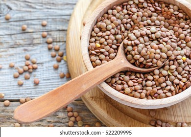 Lentils and spoon in a wooden bowl close up on an old table.