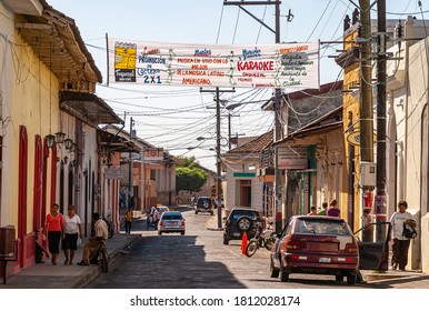 Leon, Nicaragua - November 27, 2008: White music festival banner between web of black electrical lines in light blue sky above folksy neighborhood street with people, houses, and cars.