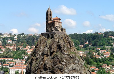 Le-Puy-en-Velay France May 2019. St Michael's chapel. In Aiguihe near town. Built 962 on volcanic formation 85 meters high. Chapel reached by 268 steps carved into rock. Blue sky, town houses in rear.