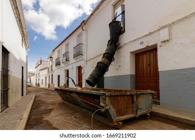 Lerena / Spain - March 05 2020: Garbage Chute For Building Waste Hangs From A Building Above A Skip On The Street In Llerena Spain