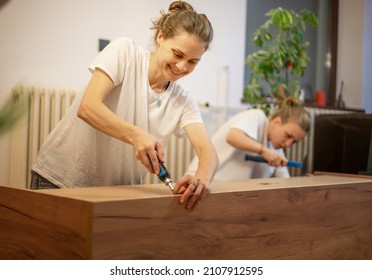 Lesbian Couple Assembling Furniture In Their New Home. Two Women Read The Cabinet Assembly Instructions.