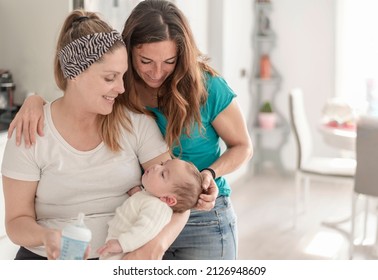 A Lesbian Couple Giving A Bottle Of Milk To Their Baby, Gay Marriage, Gay Parents And Adoption Concept