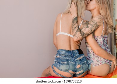 Lesbian Couple Kissing Hugging Behind Bare Buttocks Sitting On Pink Couch Rear View
