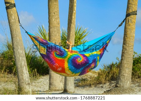 Lesbian couple relaxing in rainbow hammock at sunset. Two lesbians hid in a cozy hammock of rainbow colors on the beach. Young couple in love relaxing in hammock by beach. Lesbian couple retired.