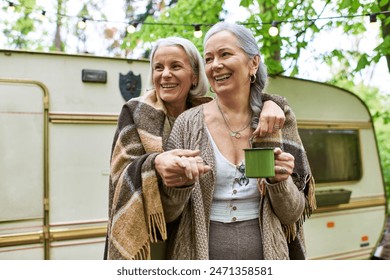 A lesbian couple smiles and embraces while camping in a green forest, enjoying the outdoors together. - Powered by Shutterstock