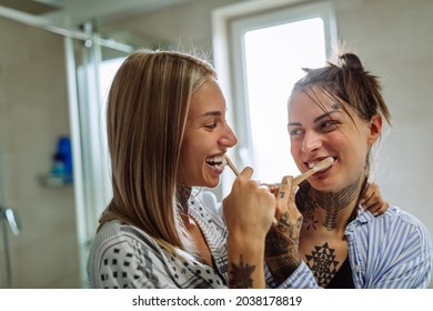 Lesbian couple wearing pajamas standing in bathroom brushing teeth in the morning - Powered by Shutterstock