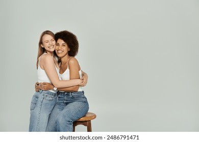 A lesbian couple in white tank tops and jeans hug and smile in a studio setting. - Powered by Shutterstock