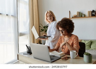 A lesbian couple works together at home, one on a laptop and the other reviewing notes. - Powered by Shutterstock