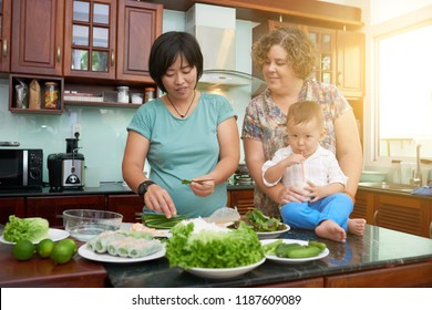 Lesbian mixed-race couple cooking healthy dish for their child in sunny kitchen - Powered by Shutterstock