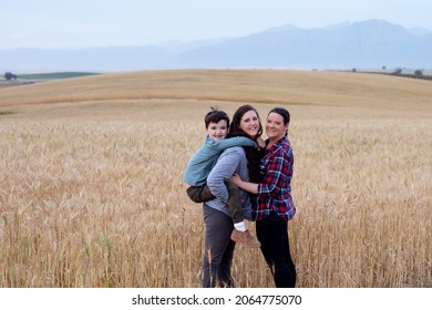 Lesbian Moms With A Young Boy. In A Wheat Field In The Country. The Boy Is Getting Piggyback From His Mother. 