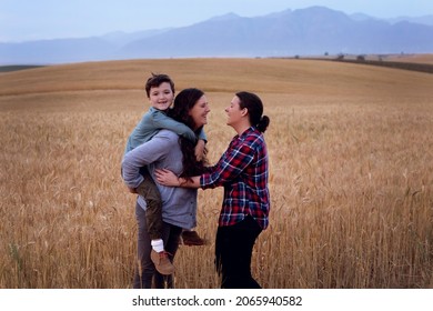 Lesbian Moms With A Young Boy. In A Wheat Field In The Country. The Boy Is Getting Piggyback From His Mother. 