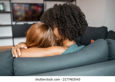 Lesbian Multiethnic Couple Watching TV Tenderly Hugging In Living Room At Home, Sweet Couple Enjoy Engaging Moment While Lying On The Sofa When Relaxed At Home. Lifestyle LGBT Family